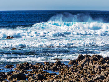 Waves splashing on rocks at beach against sky