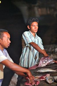 Men cutting fish on stall at market for sale at night