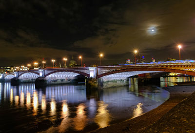 Illuminated bridge over river against sky in city at night