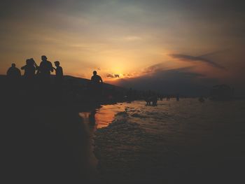 Silhouette people standing at beach during sunset