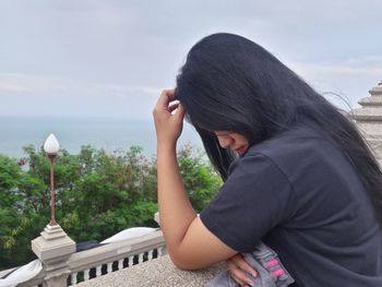 Young woman looking at retaining wall by sea against sky