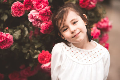 Pretty smiling baby girl 3-4 year old pose over floral roses background closeup in park. summer time