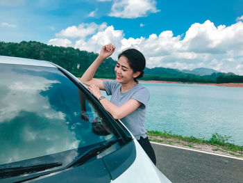 Beautiful woman in car by water against sky