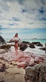 Woman standing on rock at beach against sky