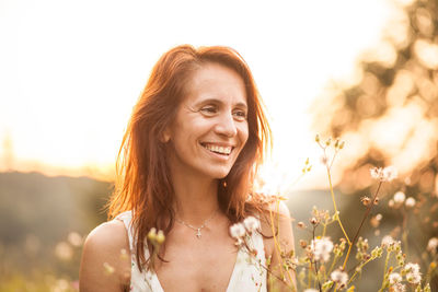 Smiling woman looking away against sky during sunset