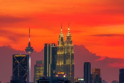 Illuminated buildings in city against orange sky