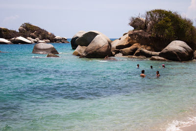 People swimming in sea by rocks