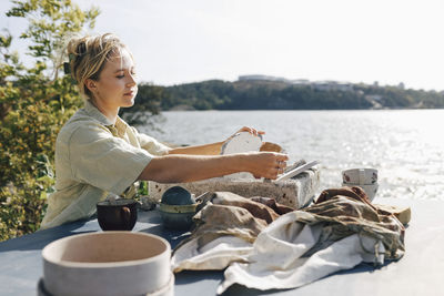 Female craftsperson drying ceramic cups on table in sunlight