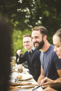 Smiling man looking away while enjoying dinner party with friends in backyard