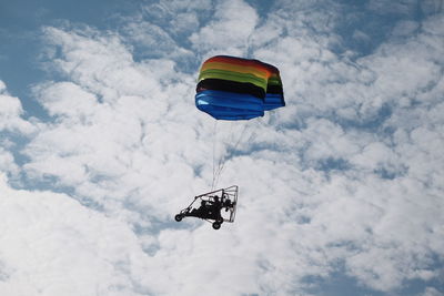 Low angle view of people powered paragliding against cloudy sky