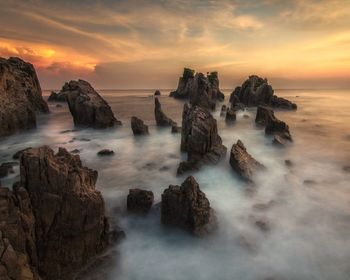 Rocks in sea against sky during sunset