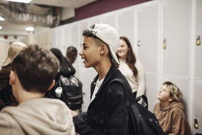 Teenage boy wearing cap by male friend in school corridor