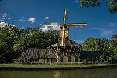 Wooden yellow windmill next to tree-lined canal at weesp. a pleasant small village in netherlands.