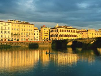 Bridge over river by buildings against sky