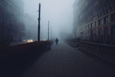 Man walking on footpath by street during foggy weather in city