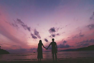 Silhouette friends standing at beach against sky during sunset