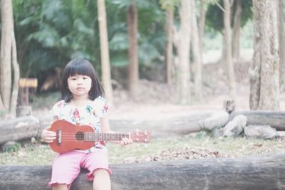 Portrait of girl playing ukulele while sitting at park