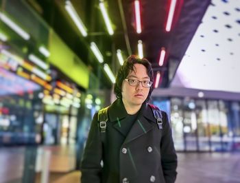 Portrait of young asian man standing against colorful neon lights and architecture.