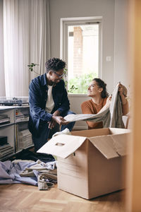 Couple talking to each other sorting out clothes from cardboard box at home