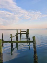 Wooden posts in sea against sky