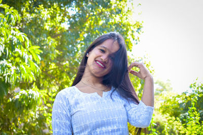 Portrait of smiling young woman against trees