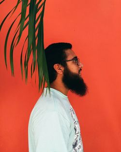 Side view of young man with beard standing against orange wall