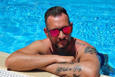 High angle view of shirtless mature man wearing sunglasses relaxing at poolside during sunny day