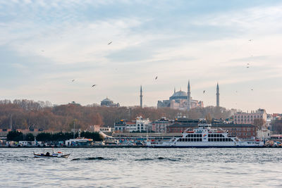 Boats in sea by buildings in city against sky