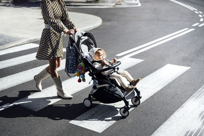 Mother with baby boy in carriage crossing street in city during sunny day