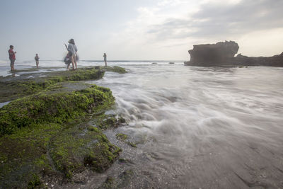 Friends standing on rock by sea against sky