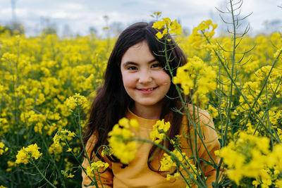 Smiling girl with long hair in yellow top stands in the field with yellow flowers