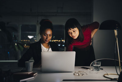 Confident female business colleagues discussing over laptop while working late at creative office