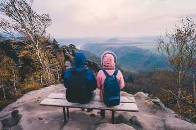 Rear view of couple sitting on mountain against sky