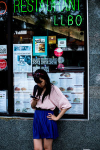 Full length of woman standing on mobile phone at store