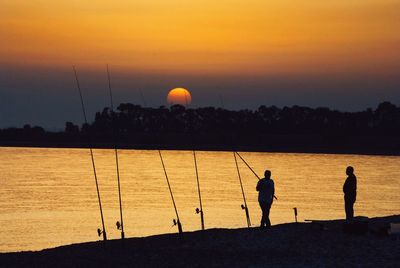 Silhouette people fishing by sea against clear sky during sunset