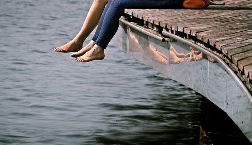 Low section of friends sitting on pier over lake