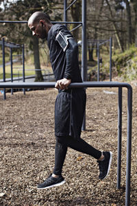 Side view of male athlete exercising on parallel bars in forest