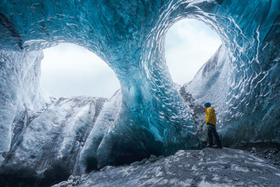 Tourist in outerwear standing near uneven holes in ice surface while exploring cave in vatnajokull glacier on winter day in iceland