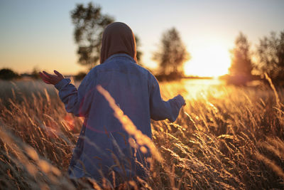 Rear view of woman standing on field against sky at sunset