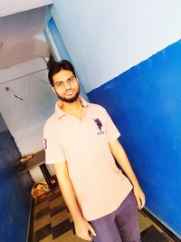 Portrait of young man standing against wall at home