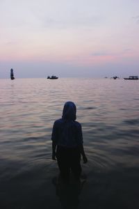 Rear view of man in sea against sky during sunset