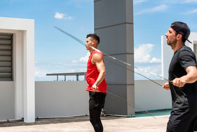 Side view of young men exercising against sky