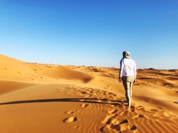 Rear view of man standing on sand at desert