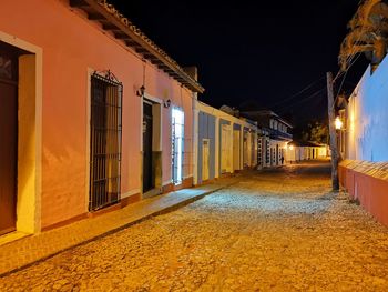 Illuminated street amidst buildings against sky at night