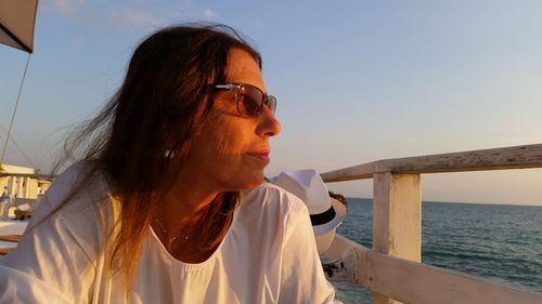 Mature woman wearing sunglasses looking at sea against sky during sunset