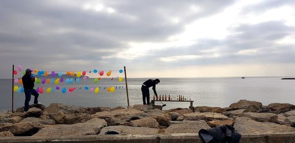 Men standing on rocks by sea against sky