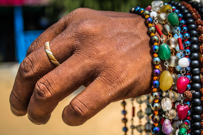 Cropped hand holding multi colored necklace in sunny day