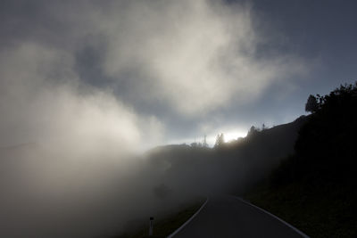 Road passing through trees against cloudy sky
