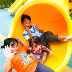 High angle view portrait of siblings sitting on slide at playground