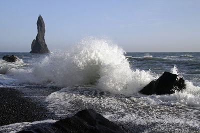 Waves splashing on rocks at shore against sky